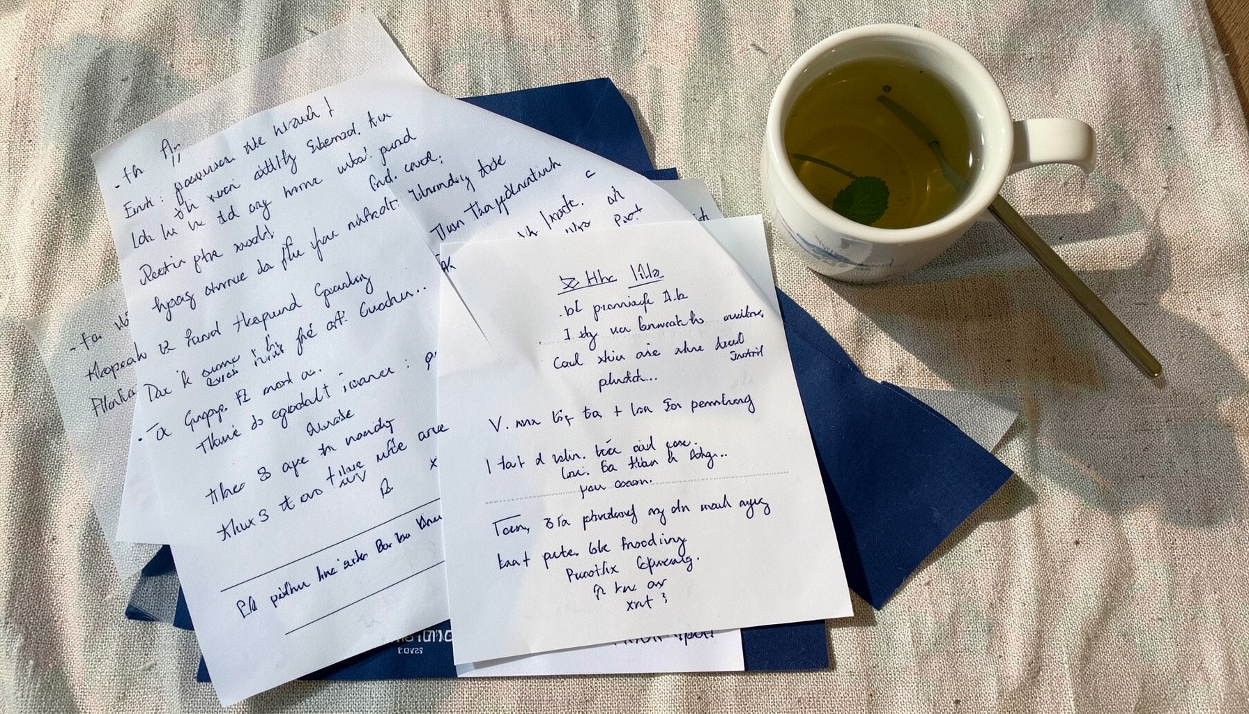 Overhead flat-lay of handwritten notes, printed event flyers, and a cup of mint tea on a textured tablecloth, warm natural mood