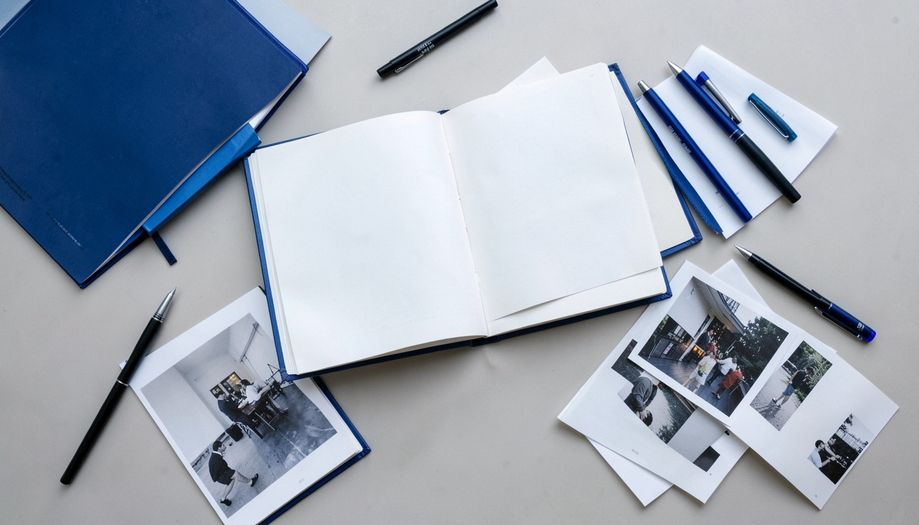 Overhead flat-lay of open notebooks, pens, and printed photographs scattered on a desk under soft daylight, reflective mood