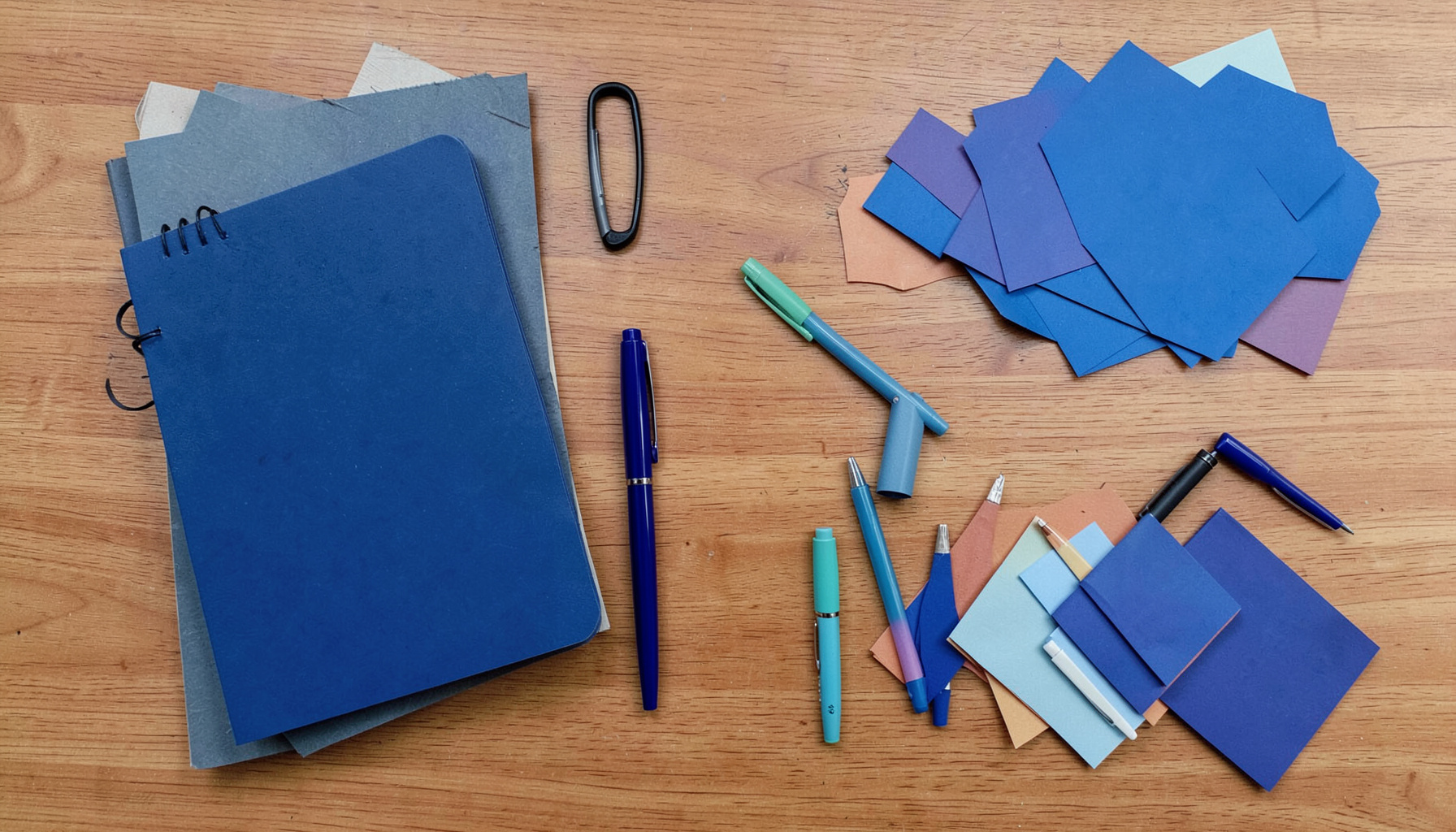 Overhead flat-lay of notebooks, pens, and colorful paper cutouts arranged on a warm wooden desk, creative planning mood